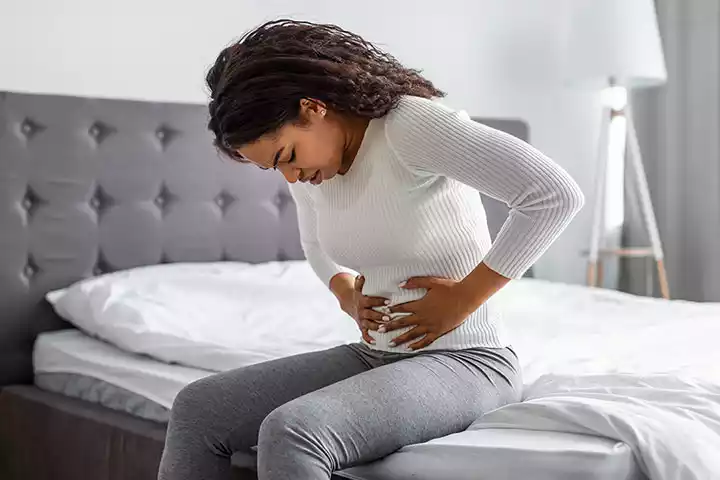 woman sitting on a bed experiencing irritable bowel syndrome
