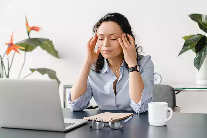 woman sitting at a work desk experiencing a headache