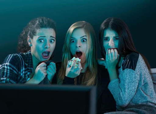 three women eating popcorn and watching a scary movie